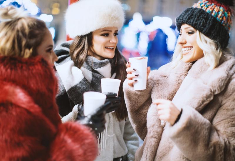 Tri ženy na vianočných trhoch s nápojom v ruke.