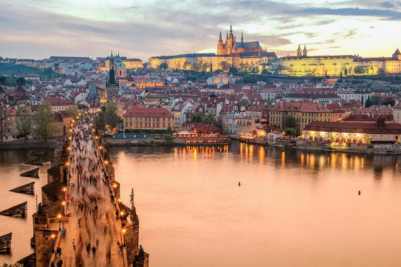 Historická Praha, s mostom, riekou a hradom v pozadí po západe slnka.