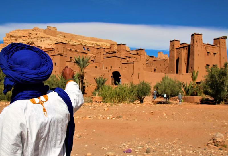 Kasba Ait Benhaddou a Berber v tradičnom odeve ukazujúci na filmové mesto.