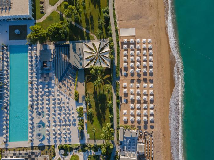 Piesočnatá pláž a krásne tyrkysové more Tureckej riviéry s hotelom a bazénom.
