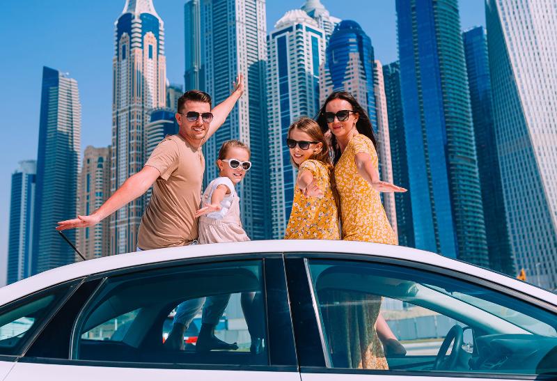 Dve deti a rodičia v aute pred mrakodrapmi v Dubaji.