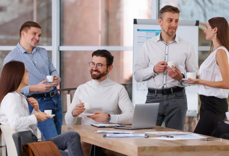 Pracovná skupina ľudí v kancelárii s kávou v ruke.