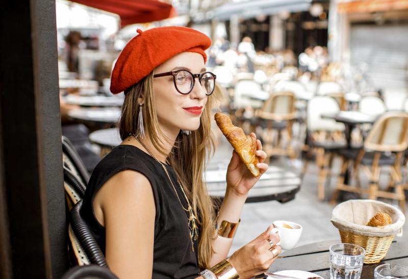 Mladá žena pije kávu a je croissant v kaviarni v meste.