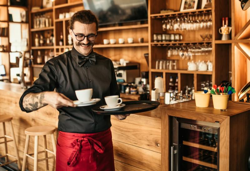 Čašník s úsmevom nesie dve kávy v kaviarni.