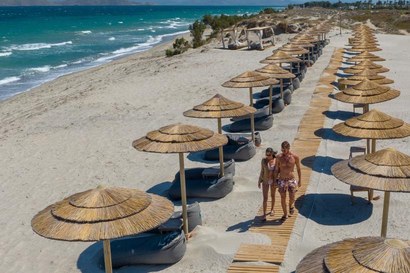 Piesková pláž, slnečníky a lehátka a pár na ostrove Kos.