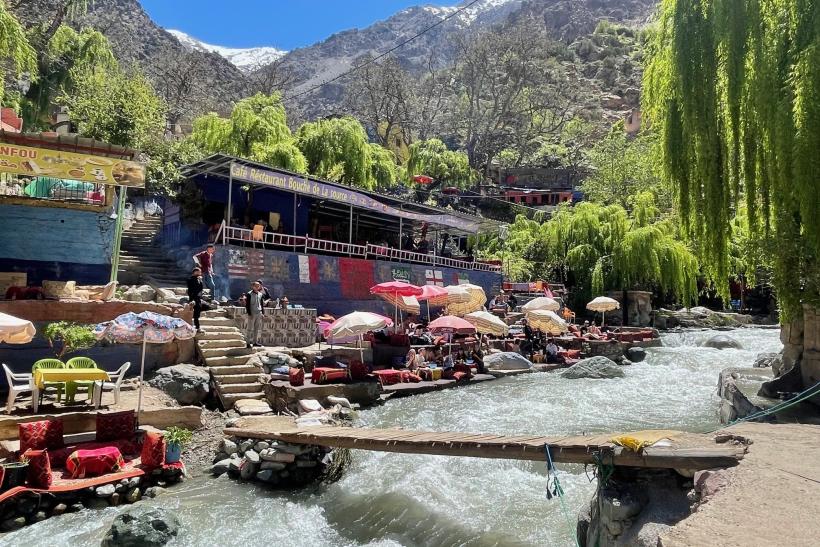 Rieka, stoly a stoličky a hory Atlasu v pozadí so snehom v časti Ourika v Maroku.