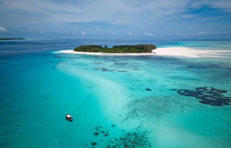 Ostrov Mnemba s tropickou zeleňou, tyrkysové more a loďky. Zanzibar
