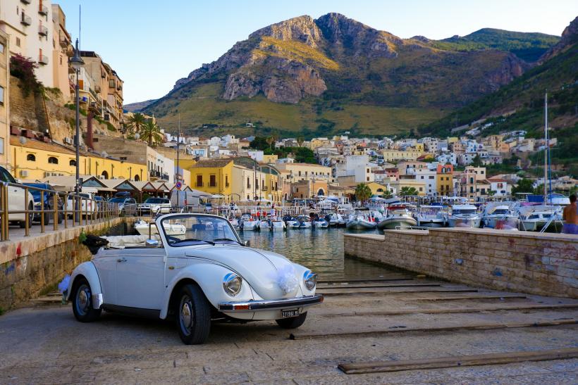 Autíčko na pobreží, domy a prístav na Sicílii.