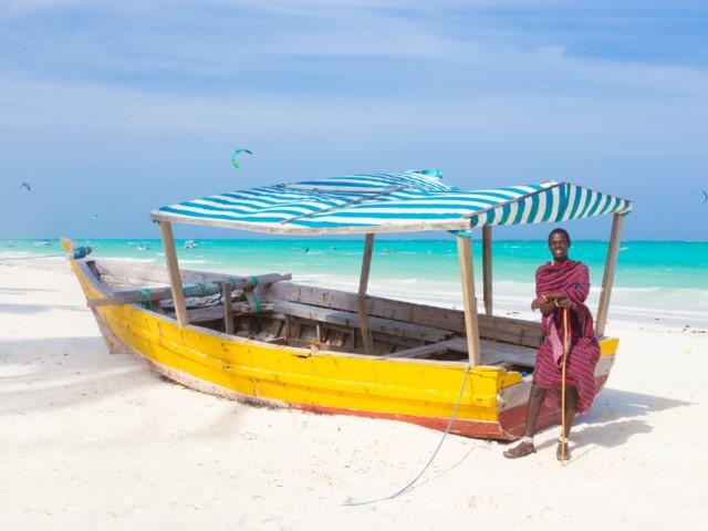 Piesková pláž, žltá loď a miestny obyvateľ. Zanzibar