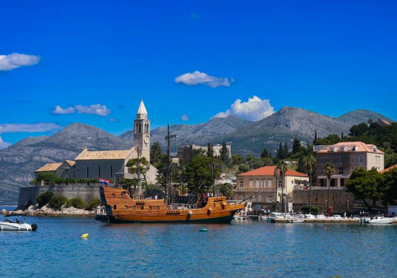 Kostol, kamenné domy a prístav s drevenou loďou na ostrove Lopud.