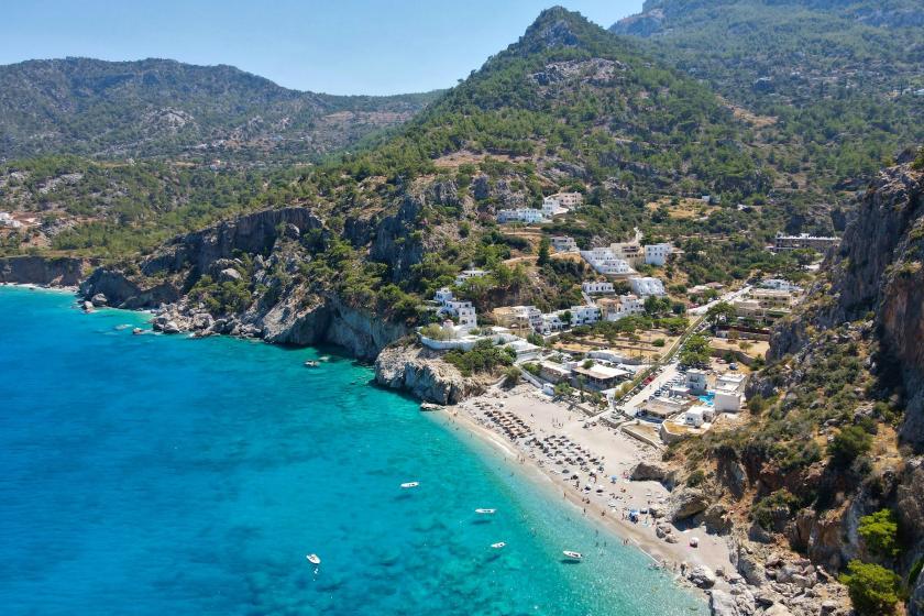 Tyrkysové more na pláži Kyra Panagia na ostrove Karpathos s okolitými kopcami s borovicami.