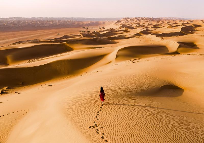 Wahiba Sands - pieskové duny a kráčajúca žena. Omán. Foto: adobe.com