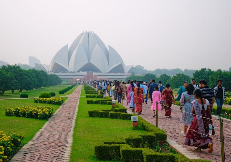 Lotus Temple v pozadí, park a kráčajúci ľudia v Indii.