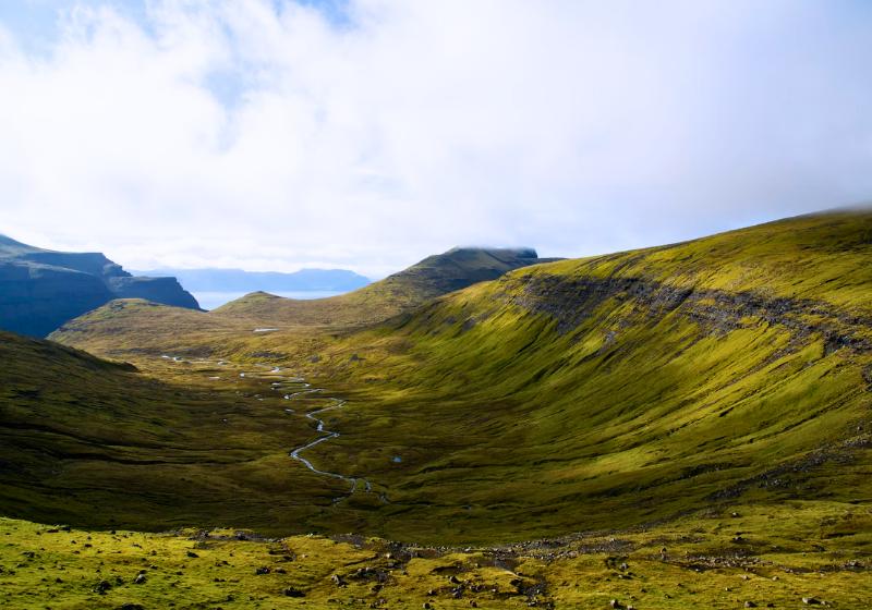 Zelené údolie, rieka, kopce a more v pozadí ostrova Streymoy, Faerské ostrovy. Foto: unsplash.com