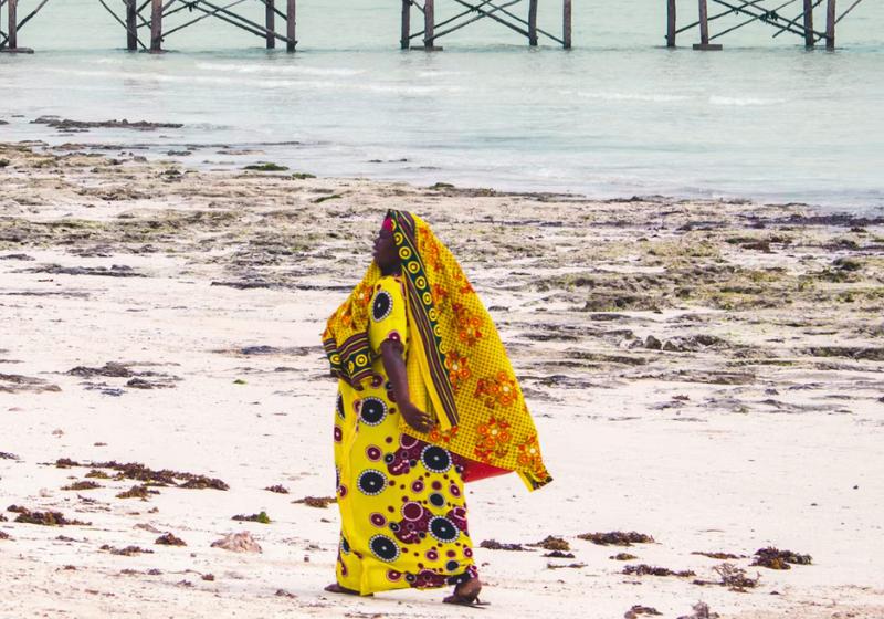 Černoška v žltých šatách na pláži na Zanzibare.