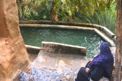 Misfat Al Abriyeen s miestnym bazénom, pri ktorom sedí žena a plamy, Omán