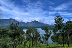 Zelený kopec, stromy, jazero a vysoké hory v pozadí počas dňa.