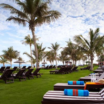 Lehátka, slnečníky, palmy a záhrada pred plážou hotela JA Beach. SAE