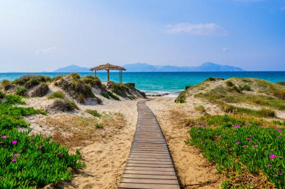 Drevený chodník cez piesočné duny k tyrkysovému moru na pláži ostrova Kos, Grécko