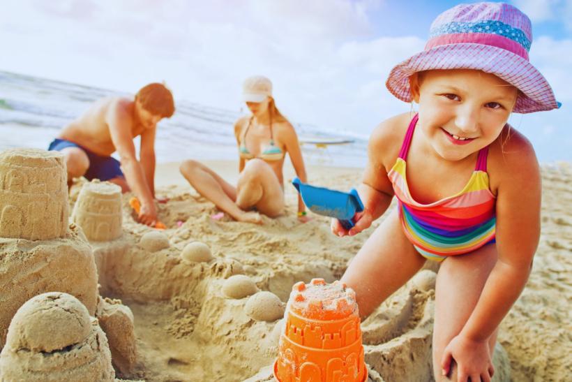 Rodinka v piesku stavia hrad pri mori na dovolenke