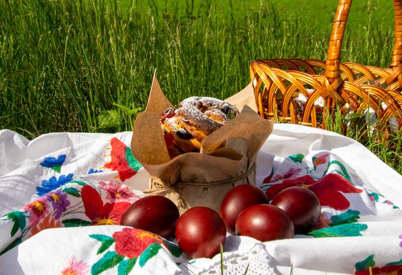 Veľkonočný piknik - košík na tráve, sladký koláč a vajíčka na obruse.