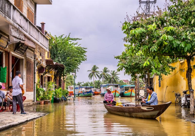 Farebné domy, chodec a ženy plaviace sa na drevenej ľodke v Hoi An vo Vietname.