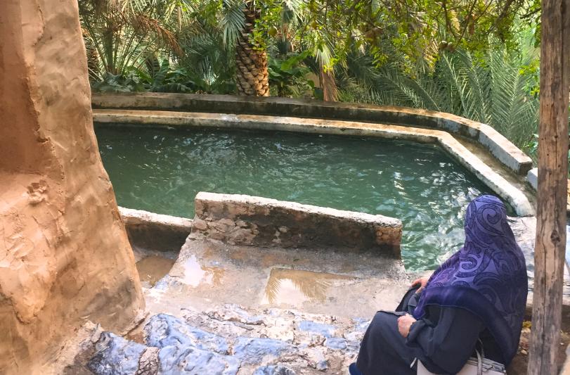 Misfat Al Abriyeen s miestnym bazénom, pri ktorom sedí žena a plamy, Omán