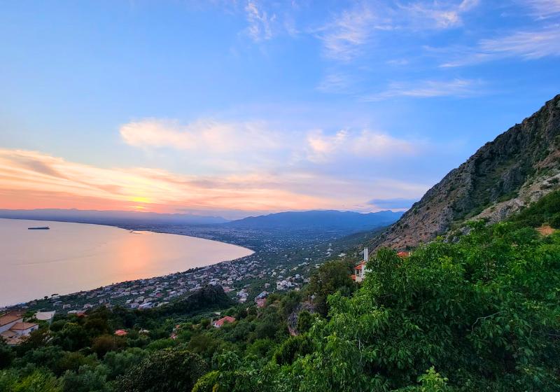 Zelené kopce, morské pobrežie a mesto Kalamata pri západe slnka. Grécko