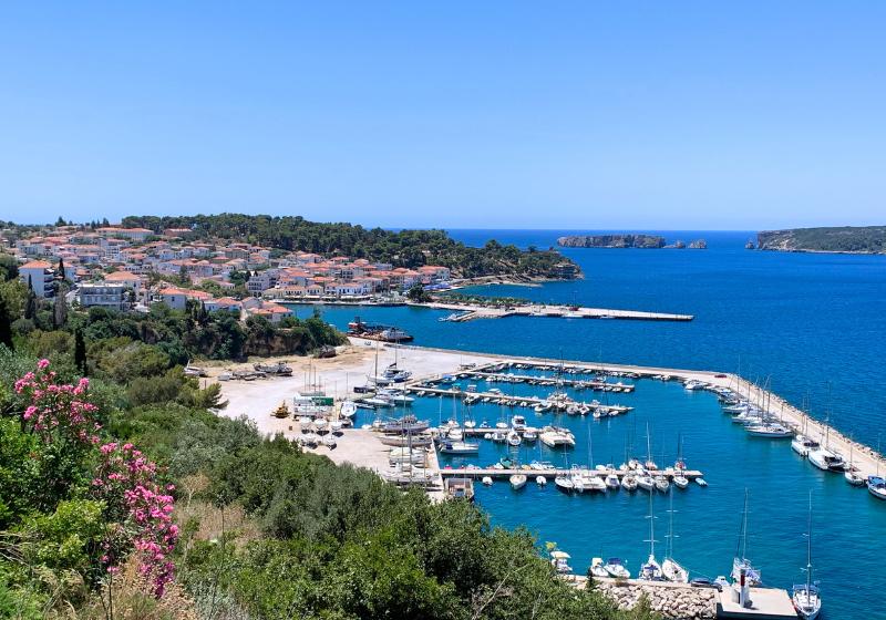 Biele domy s červenými strechami, prístav, more a zelený park.